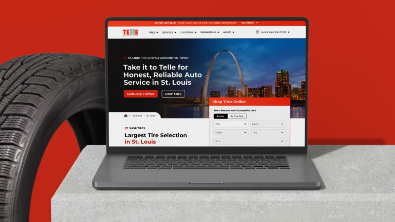 A laptop displaying an automotive service website with the St. Louis skyline. A large tire stands beside the laptop, set against a red background.