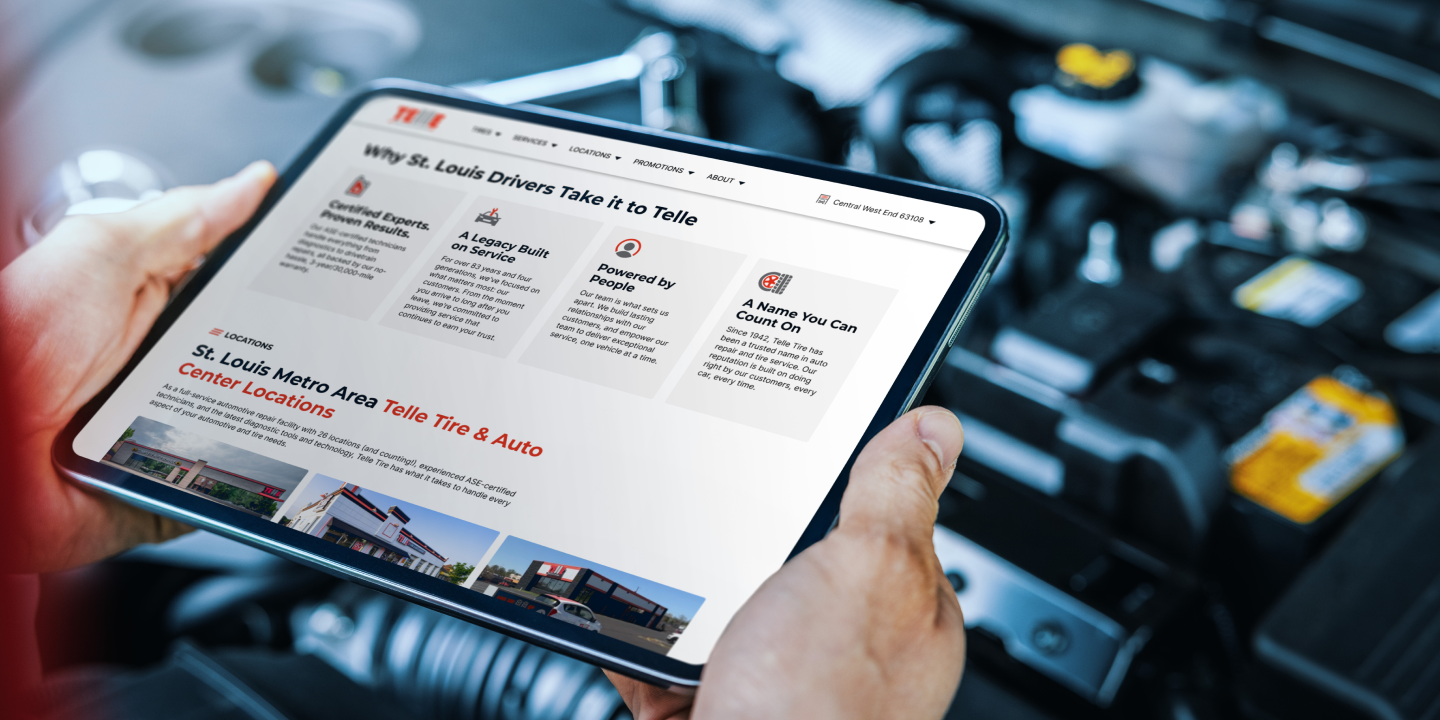 Hands holding a tablet displaying a Telle Tire & Auto website section about St. Louis service locations. The background shows a car engine in soft focus.